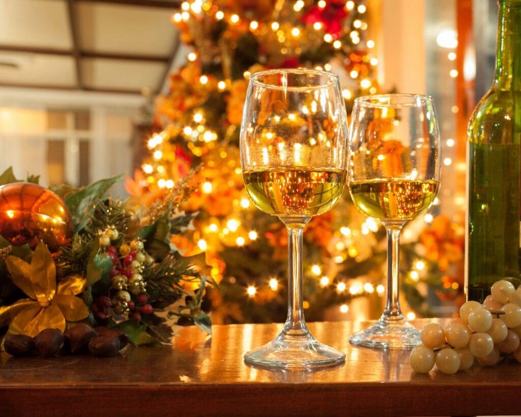 Two wine glasses are on a table in front of a christmas tree.