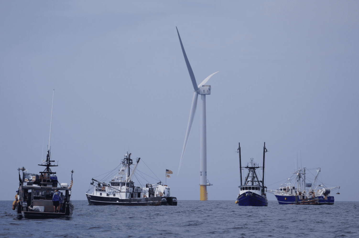 A group of boats in the ocean with a wind turbine.