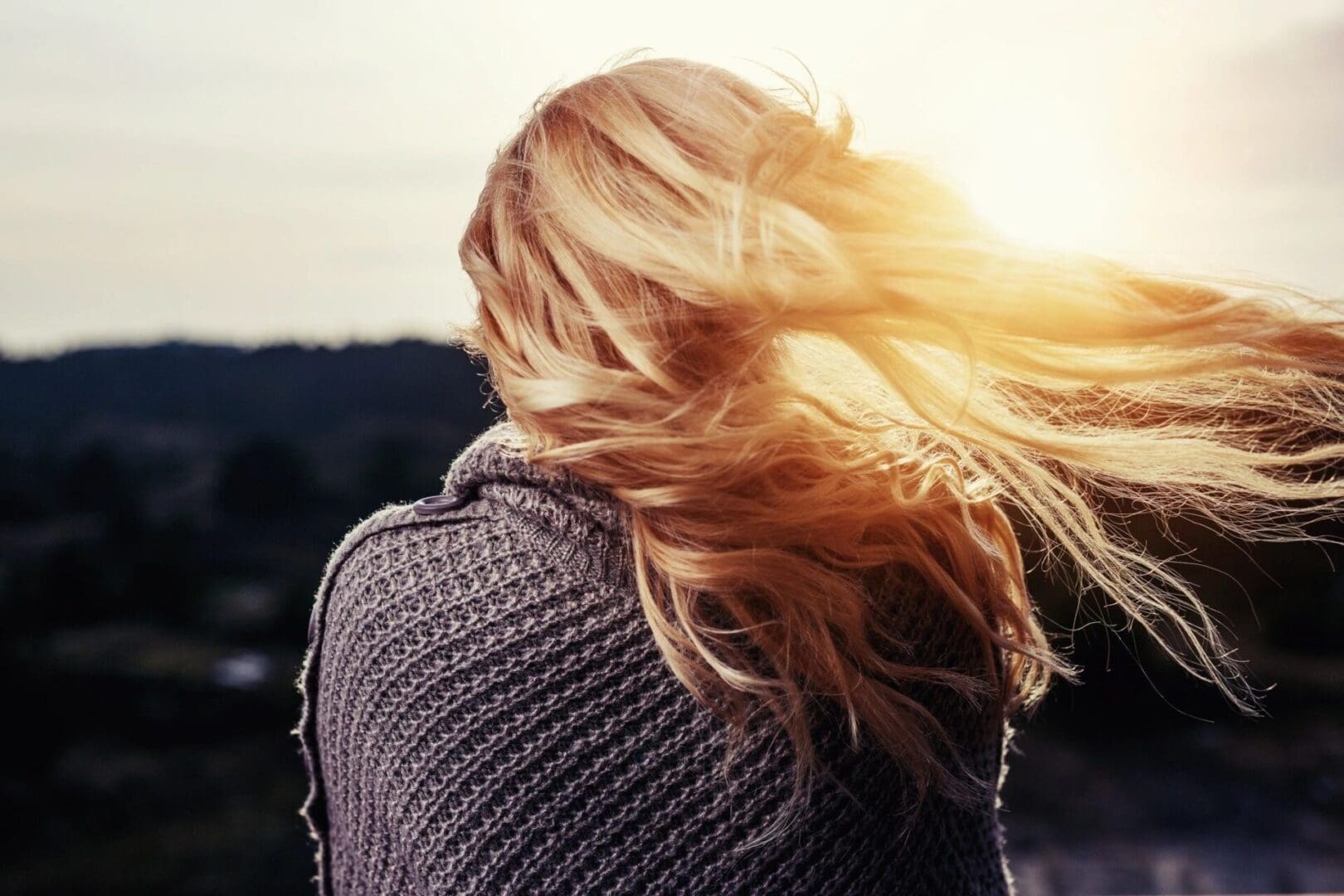 A woman with long blonde hair is looking out at the sun.