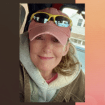 Woman smiling, wearing cap and sunglasses.