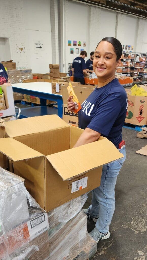 Woman smiling while packing items into boxes at a volunteer event.