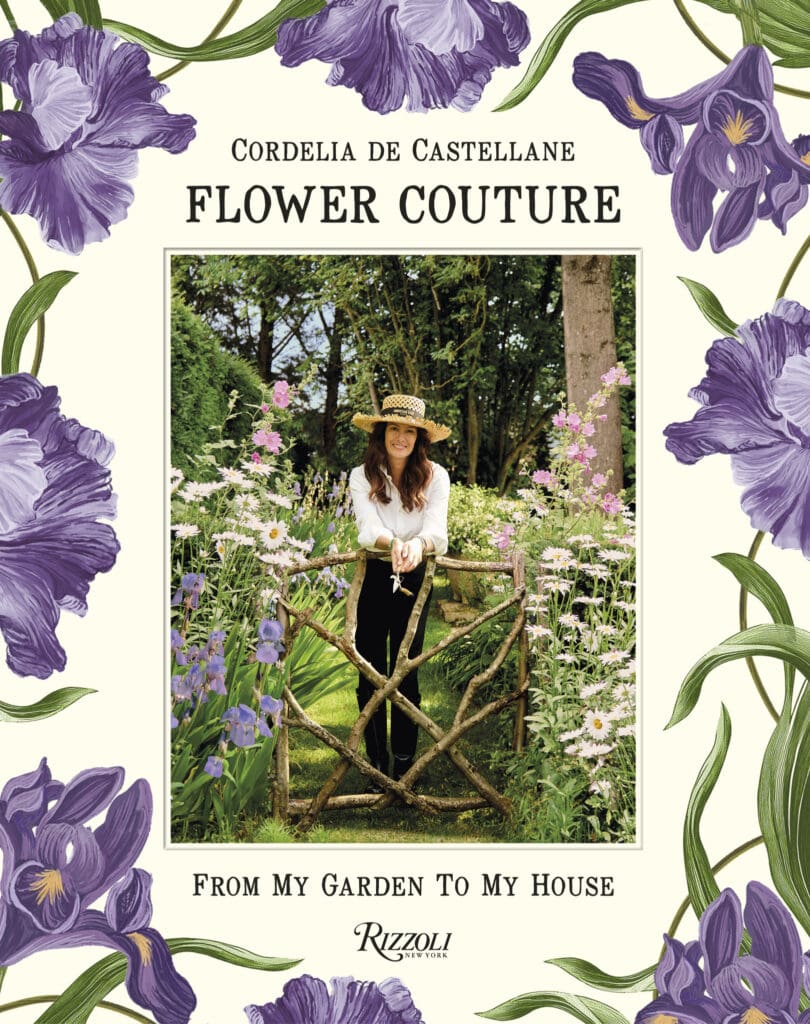 A woman standing in front of flowers and trees.