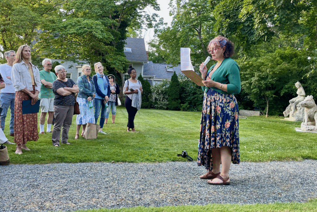 A woman standing in the grass holding papers.