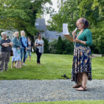 A woman standing in the grass holding papers.