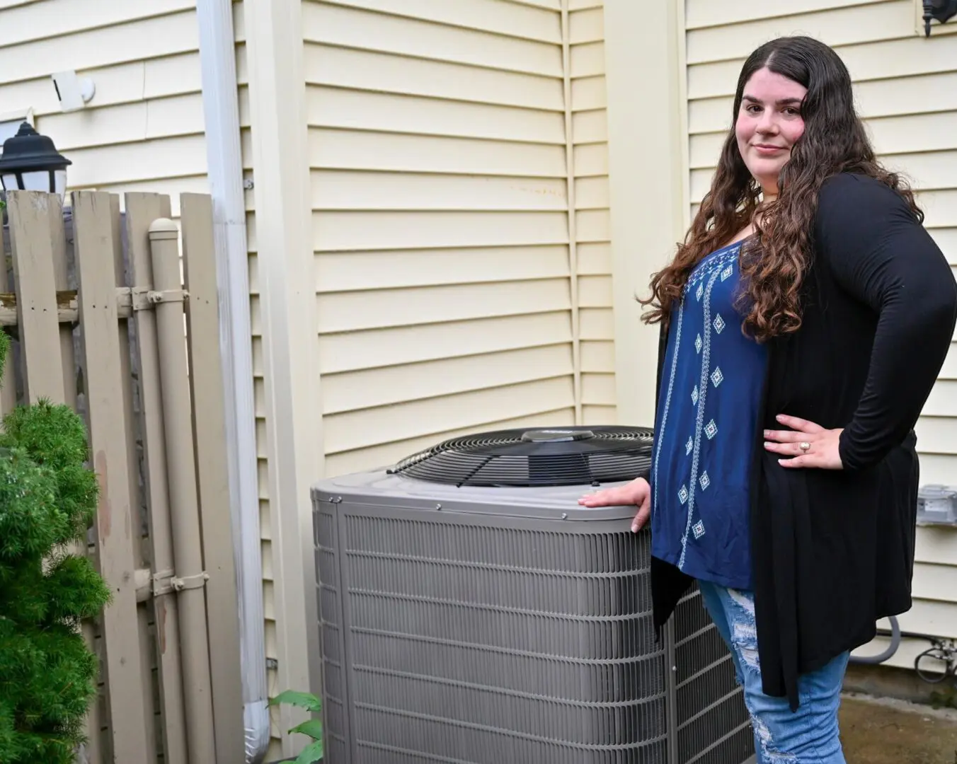 home_heatpump_w_customer A woman standing next to an air conditioner.