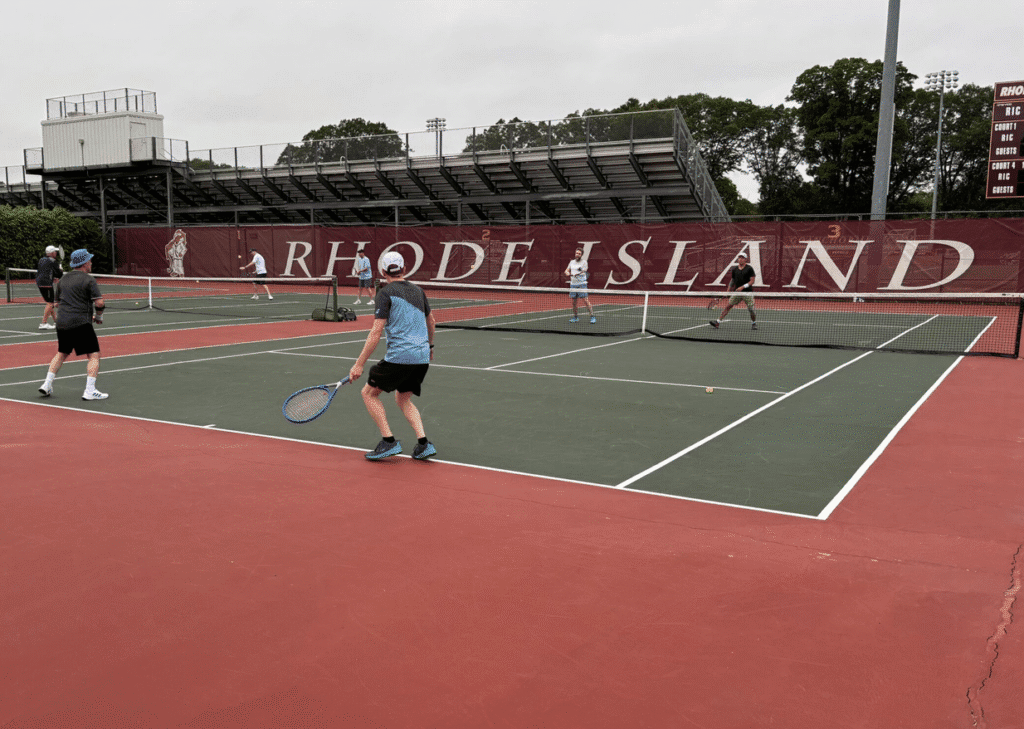 Players compete on a Rhode Island tennis court under cloudy skies.