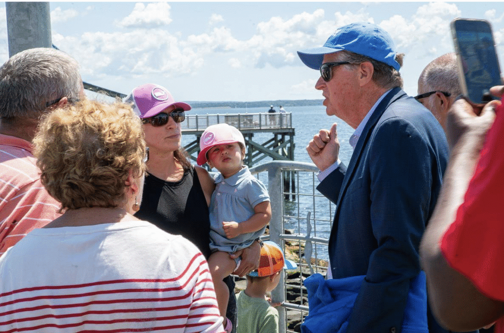 People conversing near a waterfront with a bridge in the background.