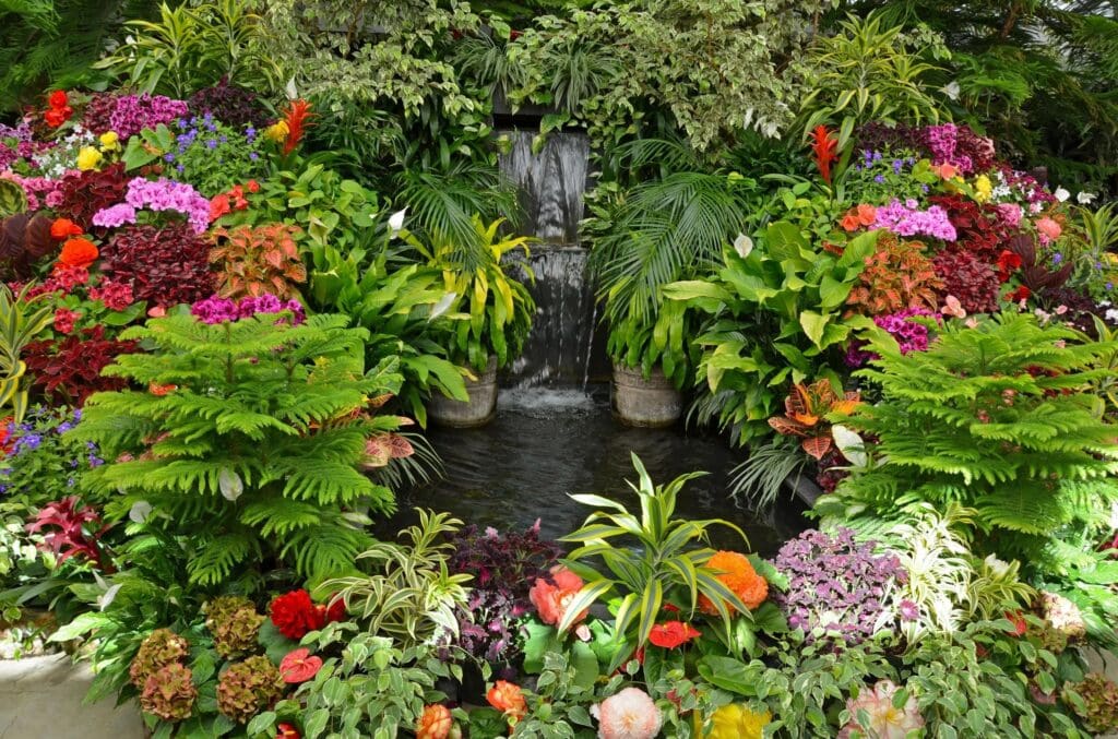 A vibrant garden with a small waterfall and diverse colorful flowers.