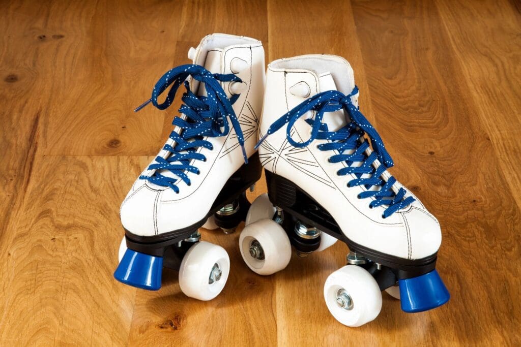 White roller skates with blue laces and wheels on a wooden floor.