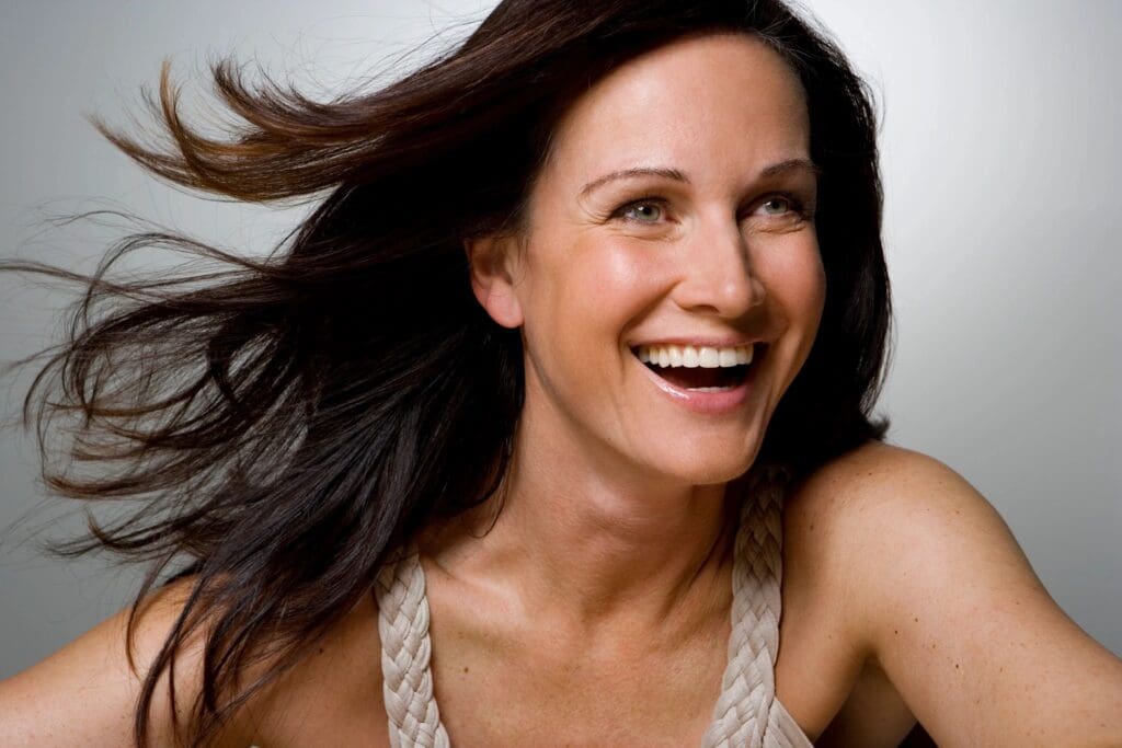 A joyful woman with flowing hair smiling brightly.