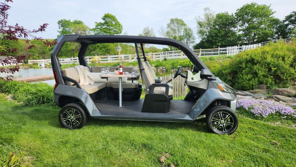 A long black golf cart with multiple seats on grass near a fence.