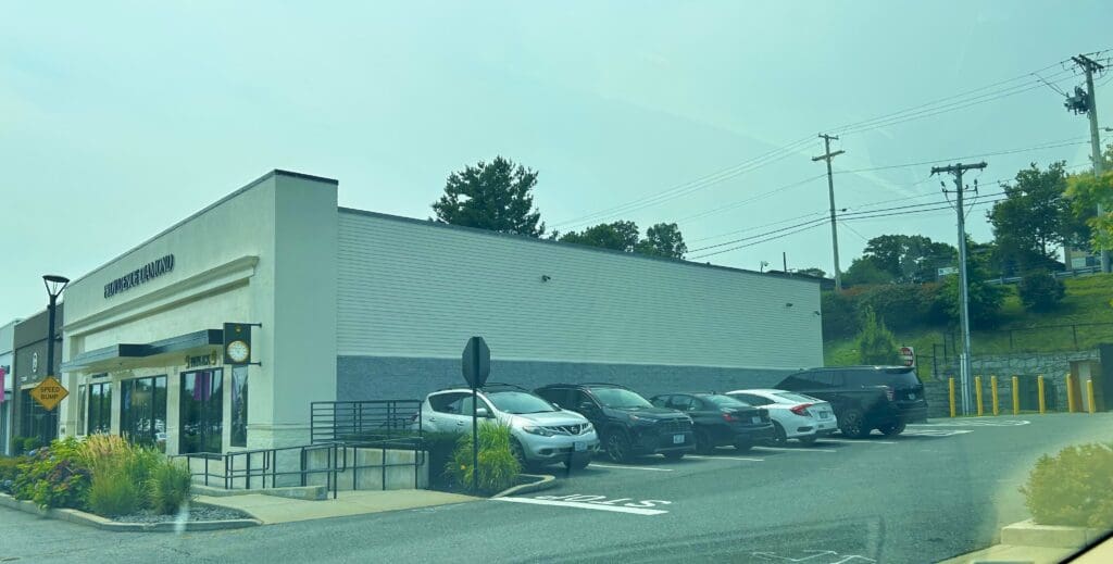A row of parked cars along a street beside a plain white building.