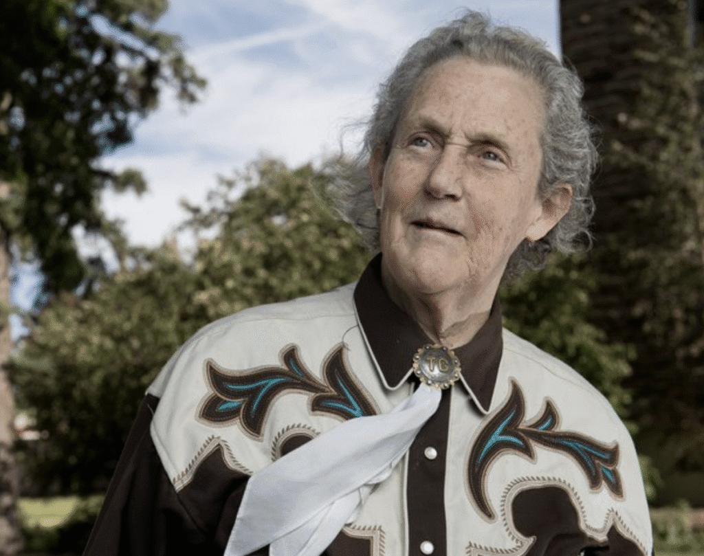 An older man in a western-style shirt outdoors holding white flowers.