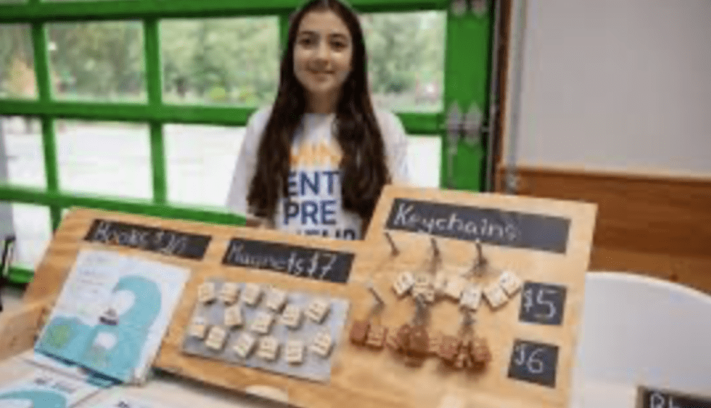 Girl stands behind a table selling jewelry and crafts.