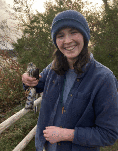 A smiling woman holding a small bird outdoors.