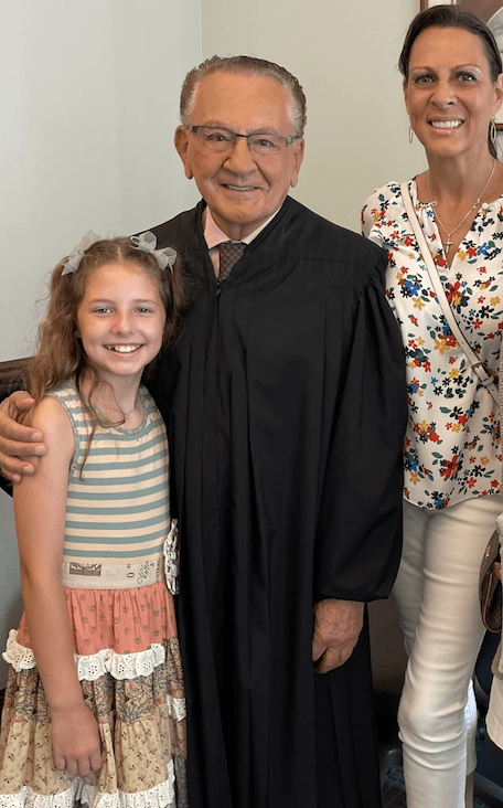 A young girl smiles next to a man in a judge's robe.