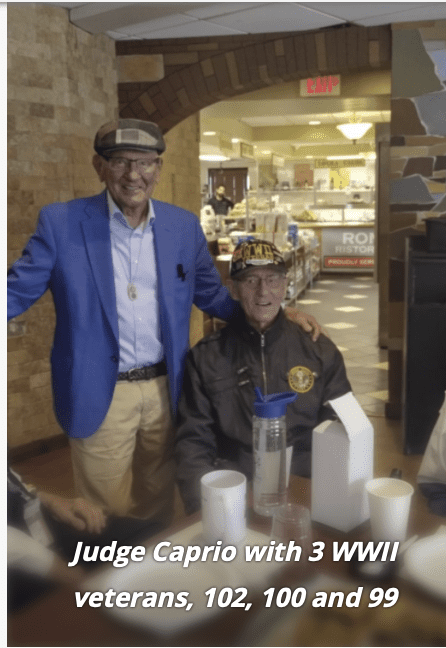 Two men smiling indoors, one standing and one seated.