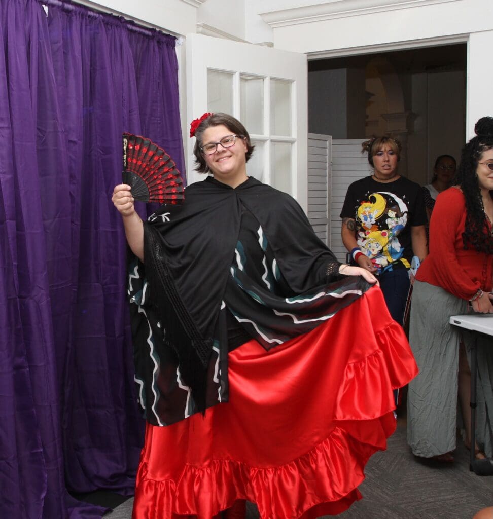 Person in a black and red flamenco dress holding a fan, posing indoors.