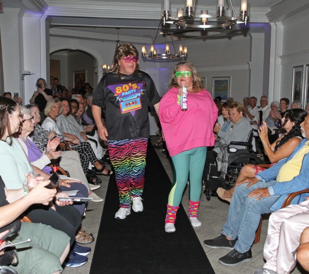 Two models walking down a runway in colorful outfits during a fashion show.