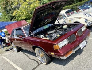 Classic maroon car with its hood open at an outdoor car show.