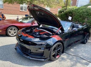 Black sports car with hood open in driveway on sunny day.