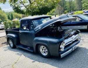 Classic black vintage pickup truck with open hood parked outdoors.