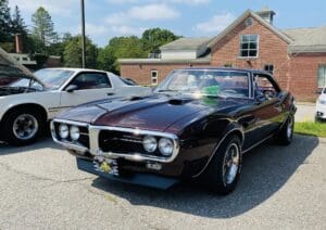 Classic black Pontiac Firebird parked outdoors near a brick building.