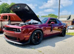 Shiny red Dodge Challenger with its hood open on a sunny day.