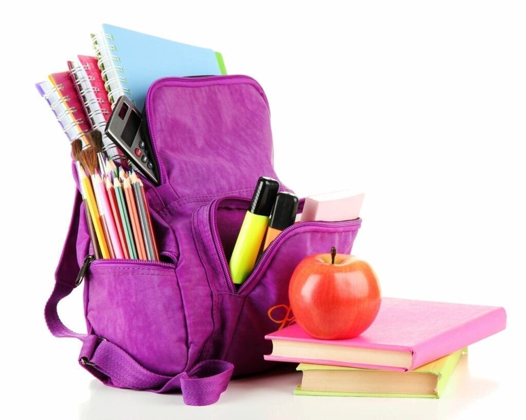 Purple backpack filled with school supplies and an apple on books.