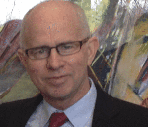 Portrait of a man wearing glasses and a suit with a red tie.