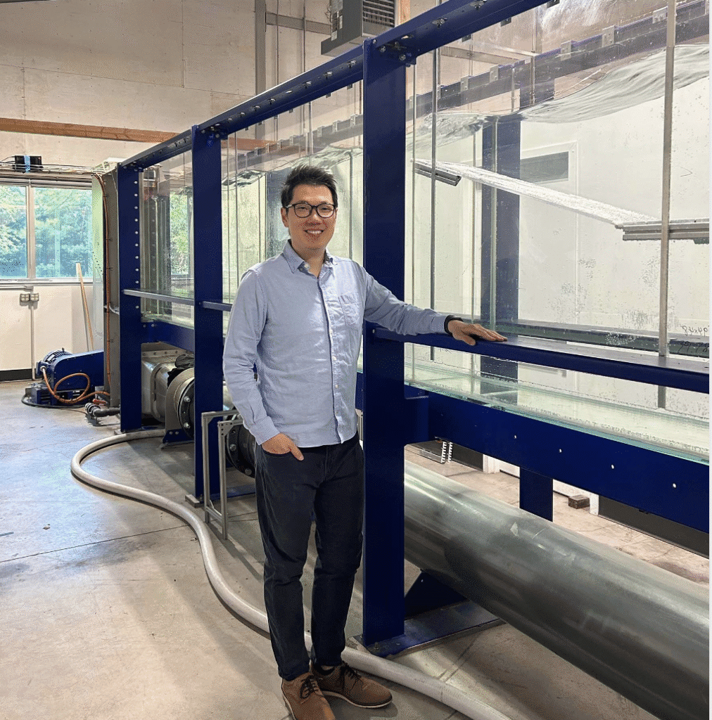 Man in business casual attire stands next to industrial equipment indoors.