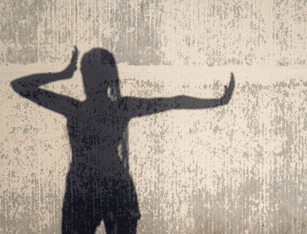 Shadow of a person with hands raised against a textured wall.