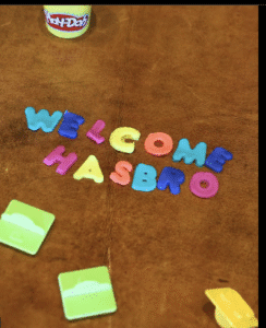 Colorful magnetic letters spelling 'WELCOME HASBRO' on a brown surface.