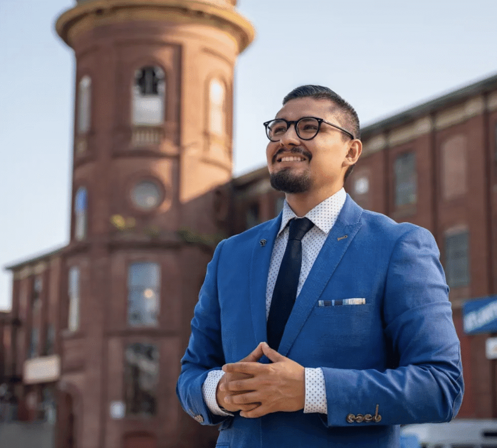 Confident man in blue suit smiling outdoors near a brick building.