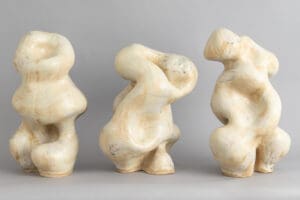 Three small abstract sculptures resembling human forms on a gray surface.