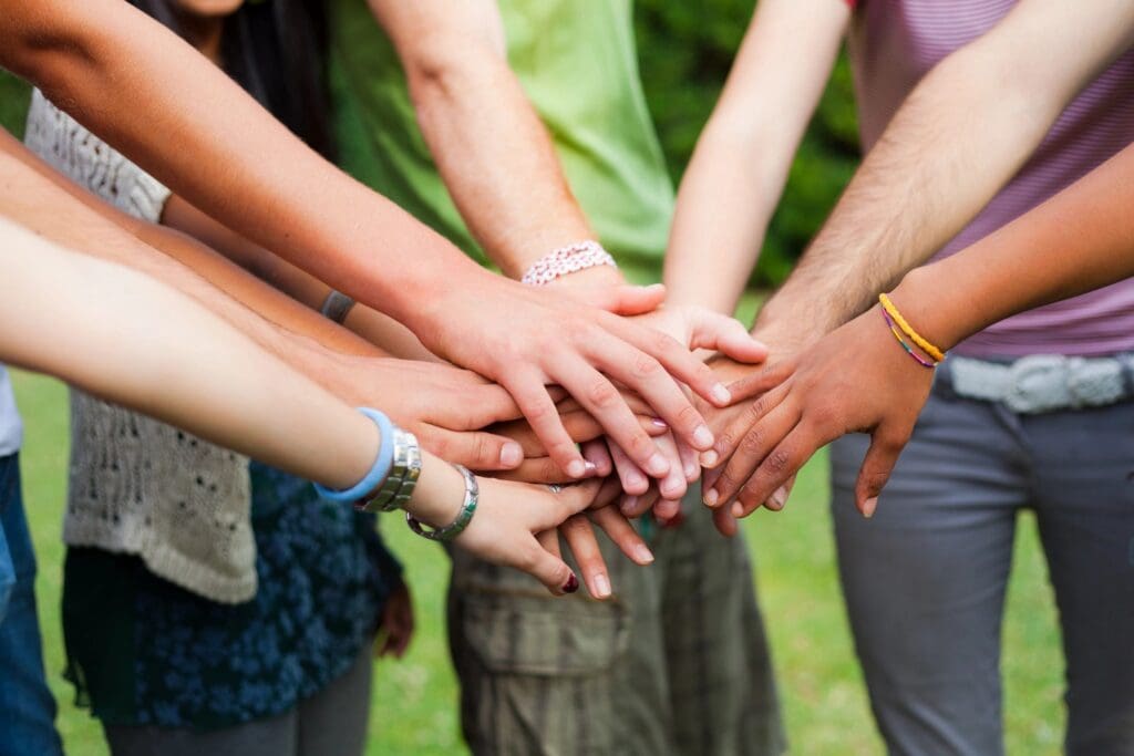 A group stacking hands in unity outdoors.