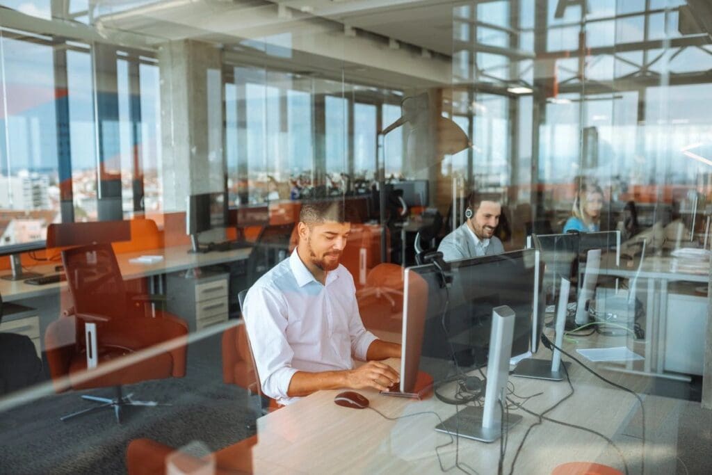 Two men working at computers in a modern office separated by glass partitions.