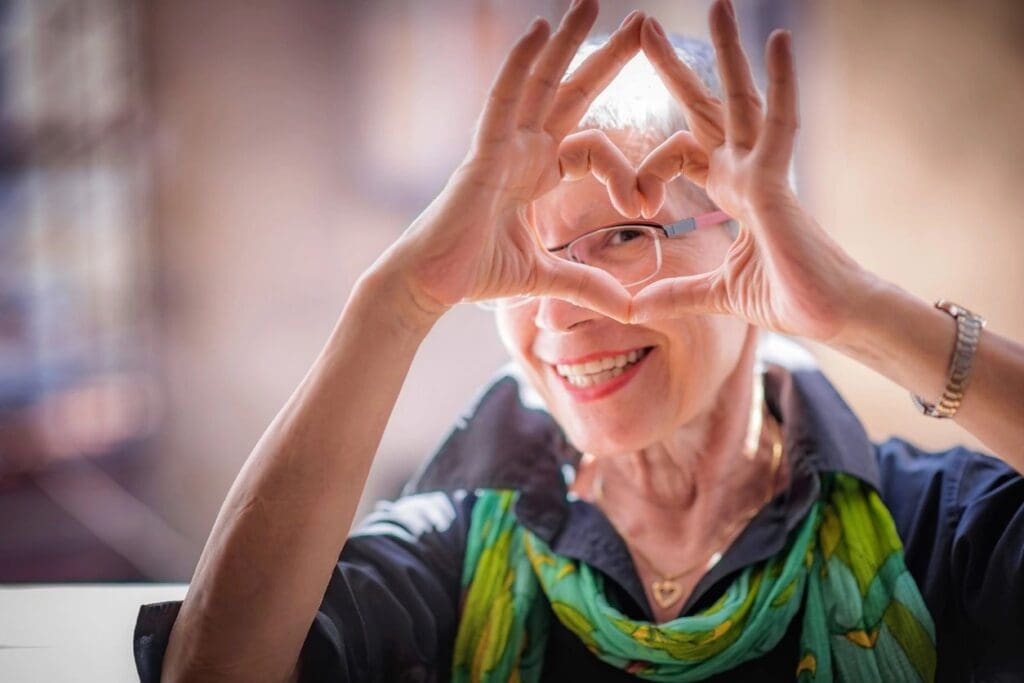 Smiling elderly woman making a heart shape with her hands.