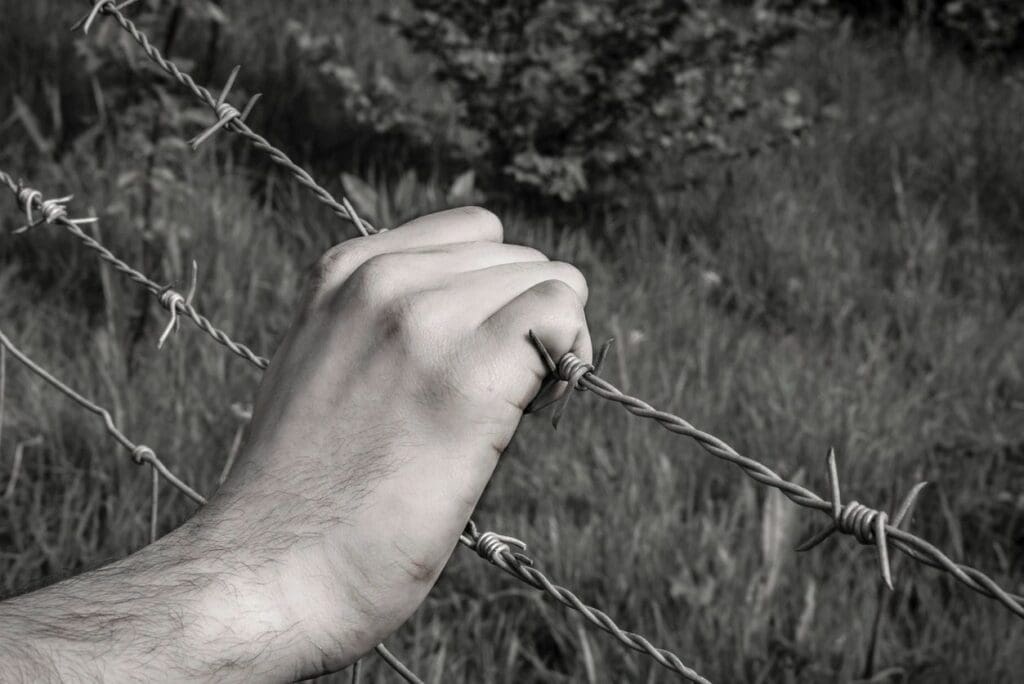 Hand gripping rusty barbed wire outdoors.