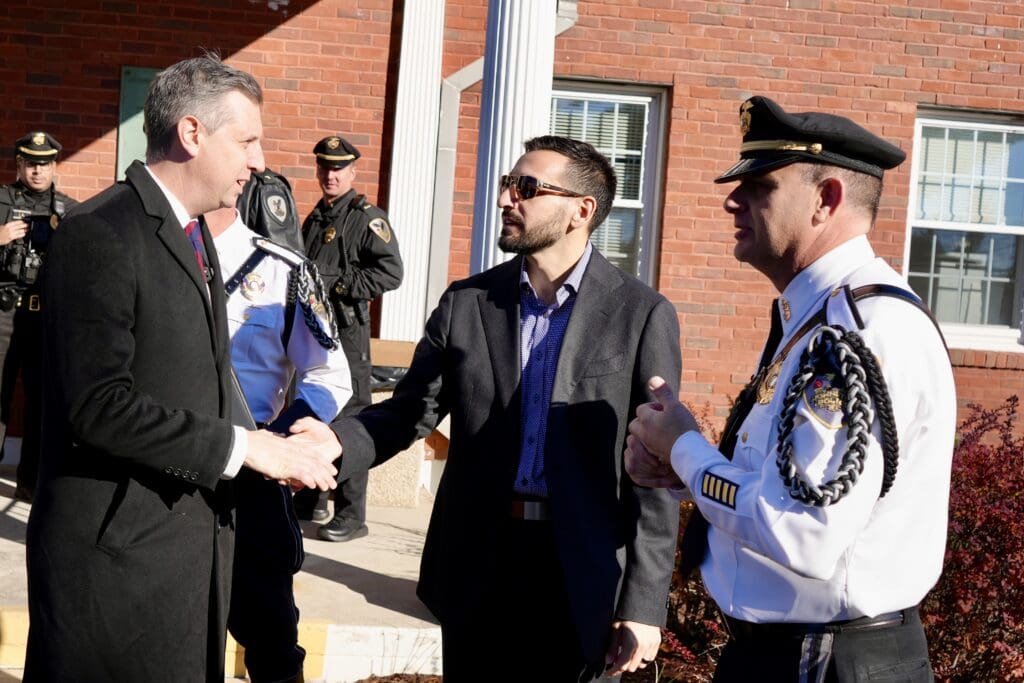 Two men shaking hands while police officers observe outside a building.