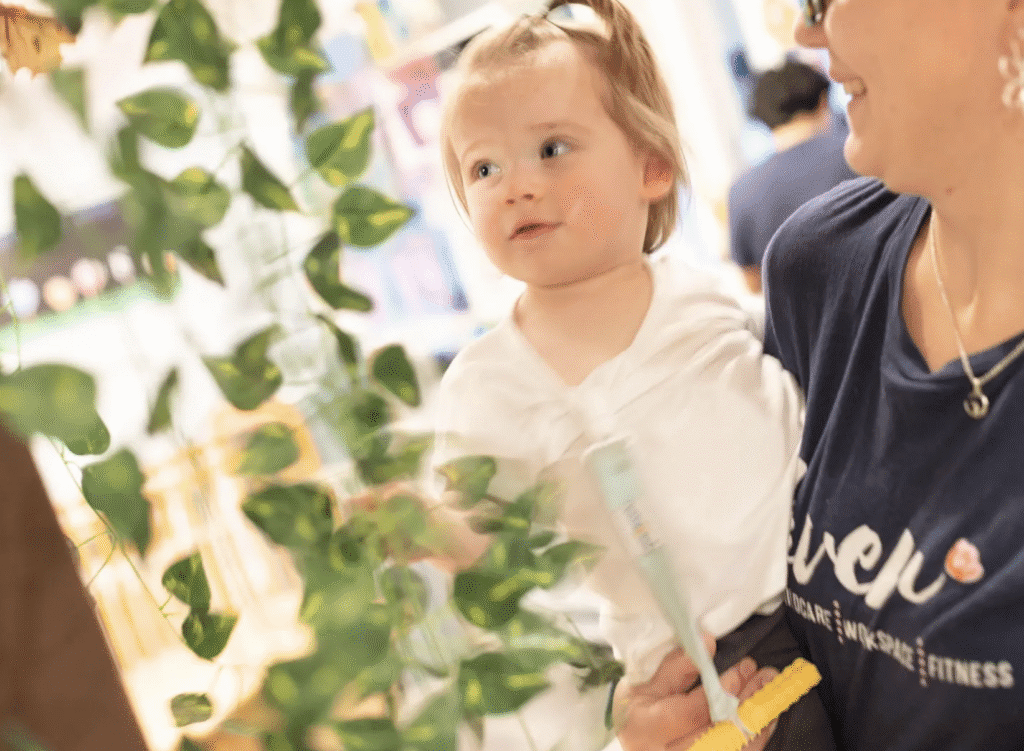 A toddler girl looking curiously at plants while holding a white flower.