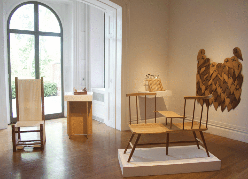 Minimalist chairs displayed in a sunlit gallery room with wooden floors.