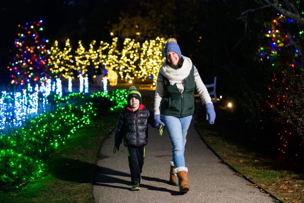 A woman and child walking together on a lit path at night.