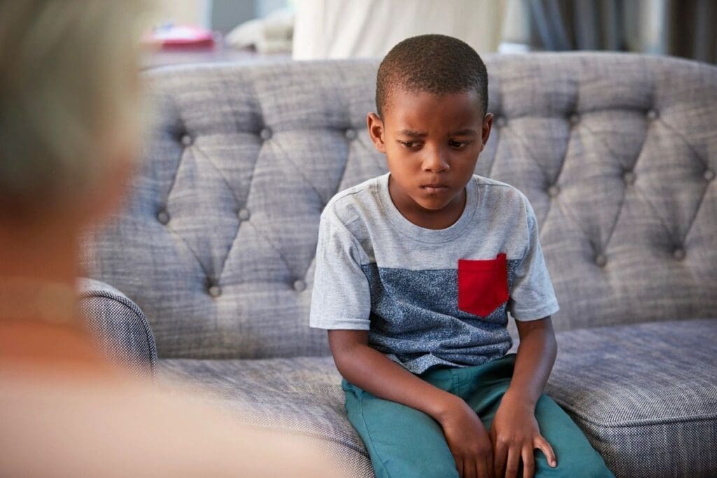A young boy sitting on a couch looking thoughtful and serious.