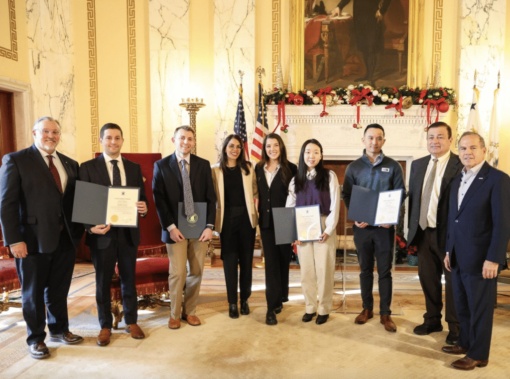 Group of six people posing with certificates and awards indoors.