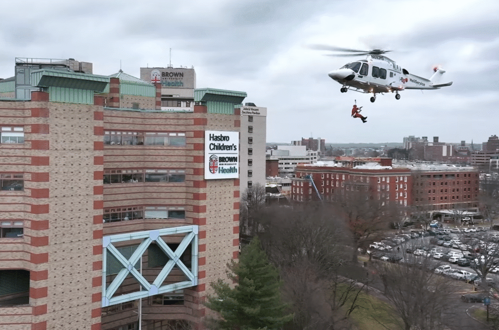Medical helicopter flying near a hospital building on a cloudy day.