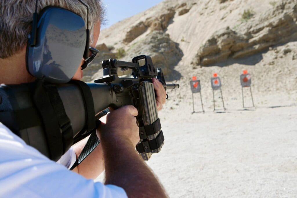 Person aiming a rifle at targets on a shooting range outdoors.