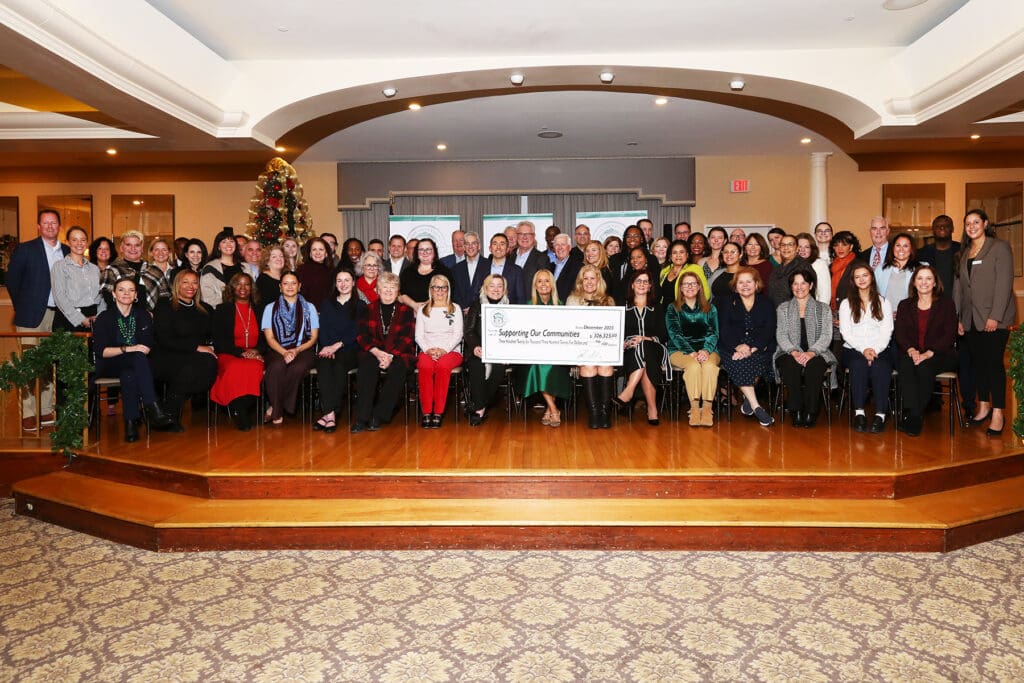 Large group posing with a giant check in a festive indoor setting.