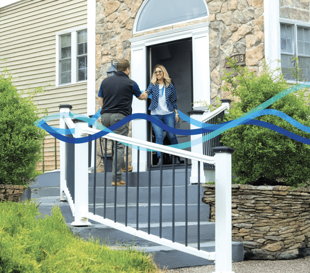 Two women greeting each other on a front porch with a blue ribbon decoration.