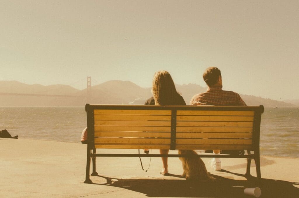 Couple sitting on a bench overlooking a calm sea at sunset.